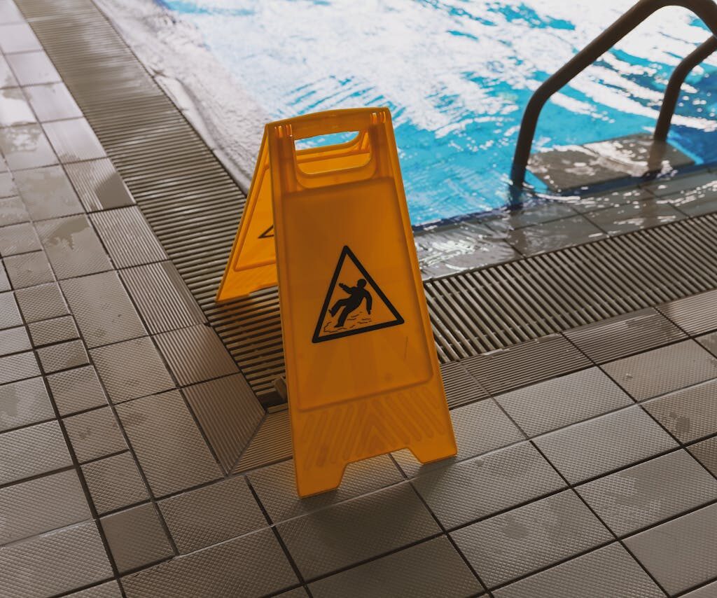 Wet floor caution sign near swimming pool edge illustrating slip and fall hazards.