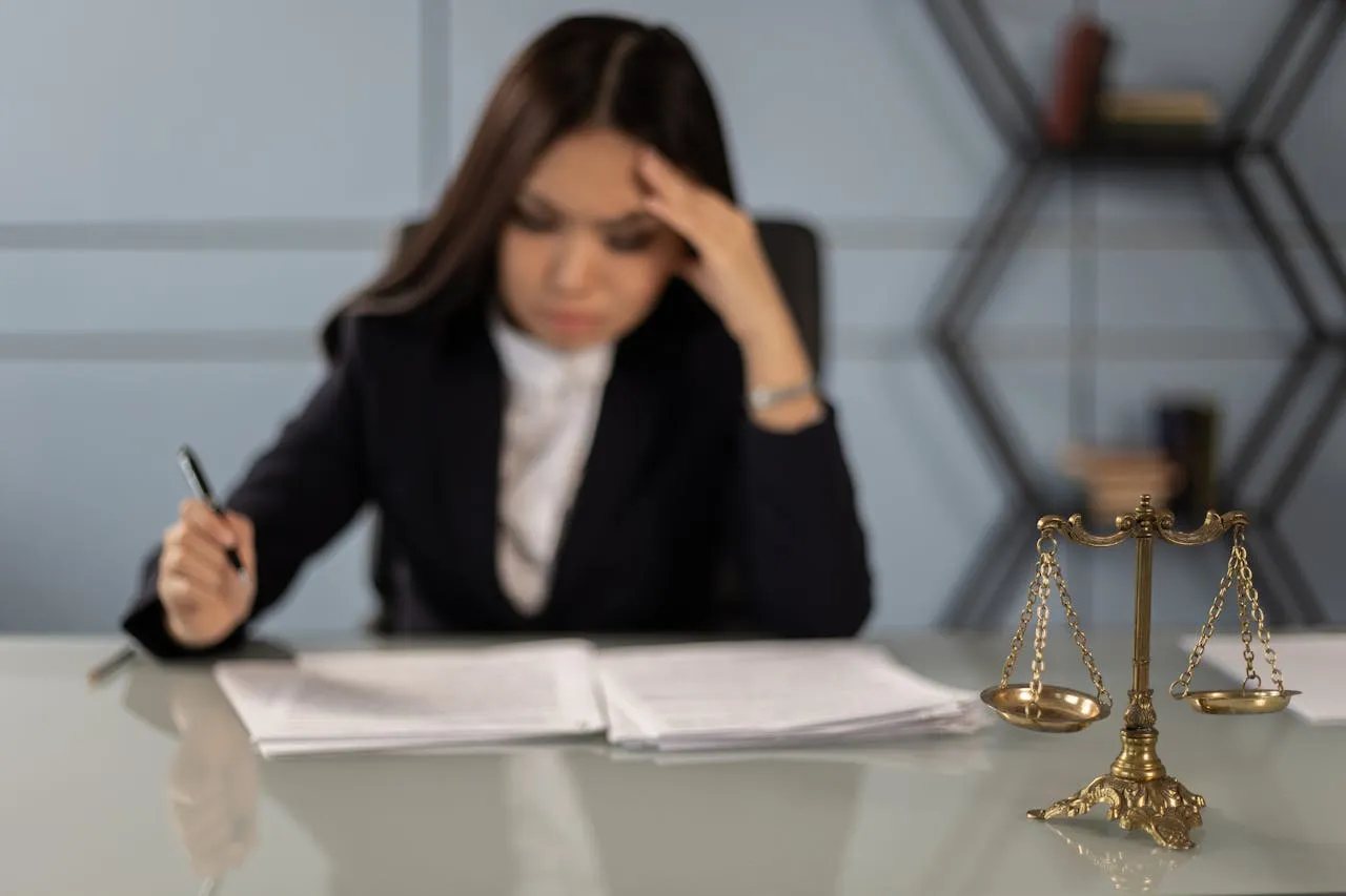Stressed lawyer reviewing documents with scales of justice in foreground.